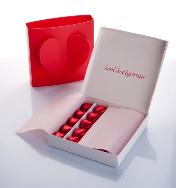 an open box with red chocolates in it on a white table next to a heart shaped container