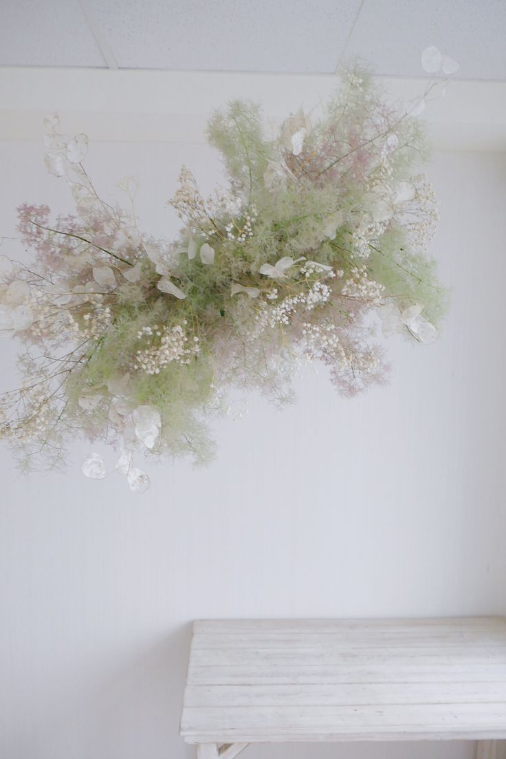 a bunch of flowers hanging from the ceiling above a white table and bench in a room