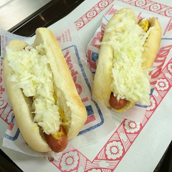 two hotdogs with sauerkraut and mustard on them sitting on wax paper