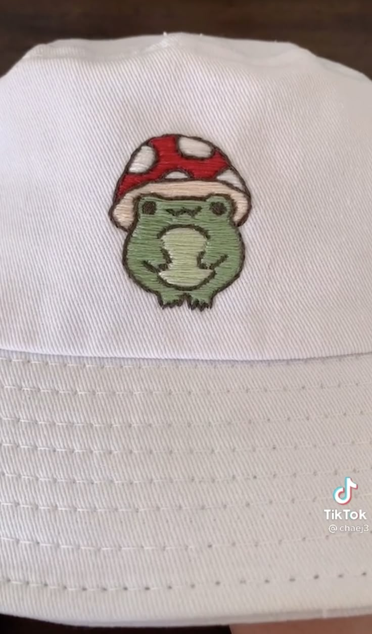 a white hat with a green frog wearing a mushroom on it