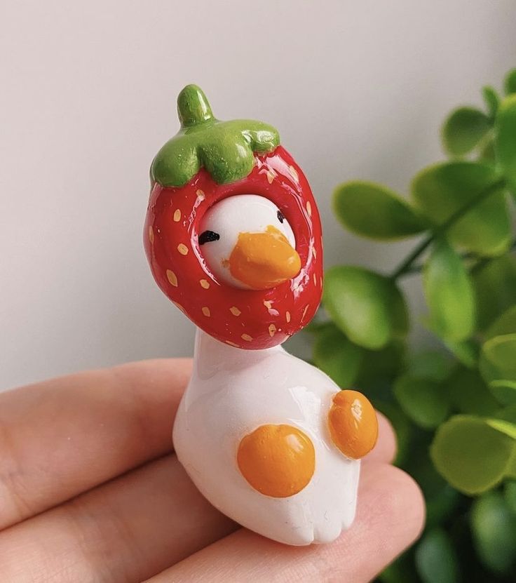 a hand holding a tiny figurine that looks like a chicken with a strawberry on its head