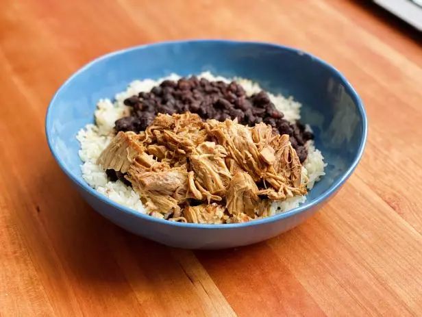 a blue bowl filled with rice and beans on top of a wooden table next to a keyboard