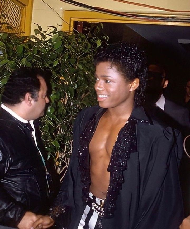 a man with no shirt standing next to another man in a black jacket and tie