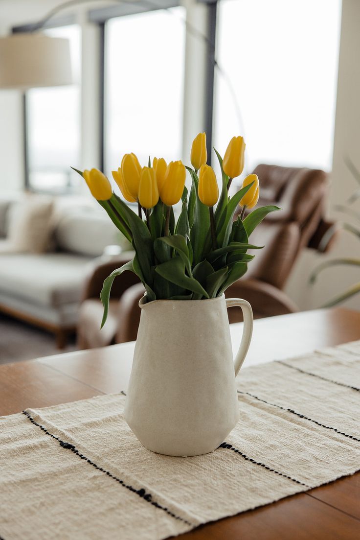 yellow tulips are in a white vase on a wooden table near a couch