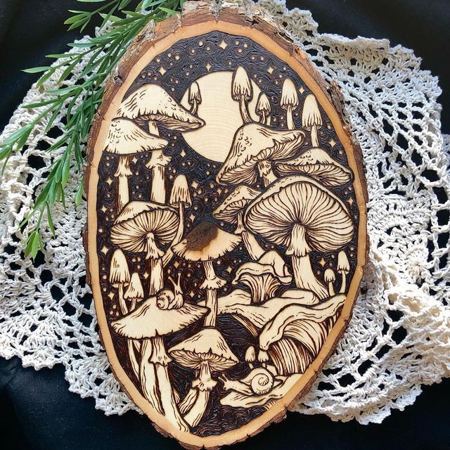 a wooden plaque with mushrooms on it sitting on top of a lace doily next to an evergreen branch