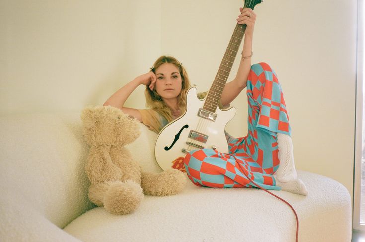 a woman sitting on a couch with a guitar and teddy bear