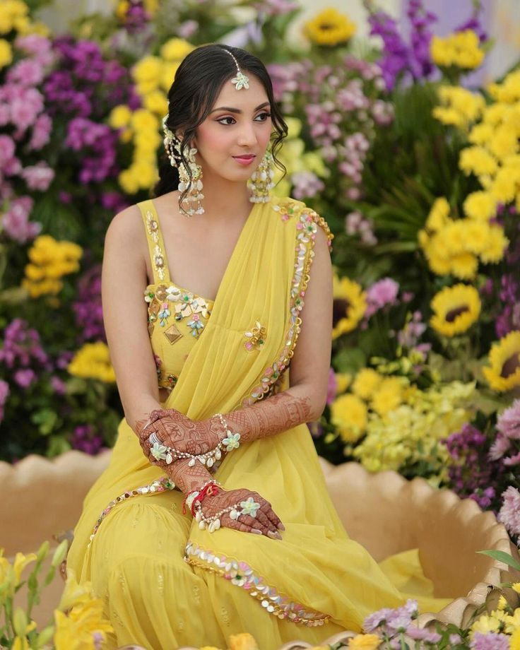 a woman sitting in front of flowers wearing a yellow dress