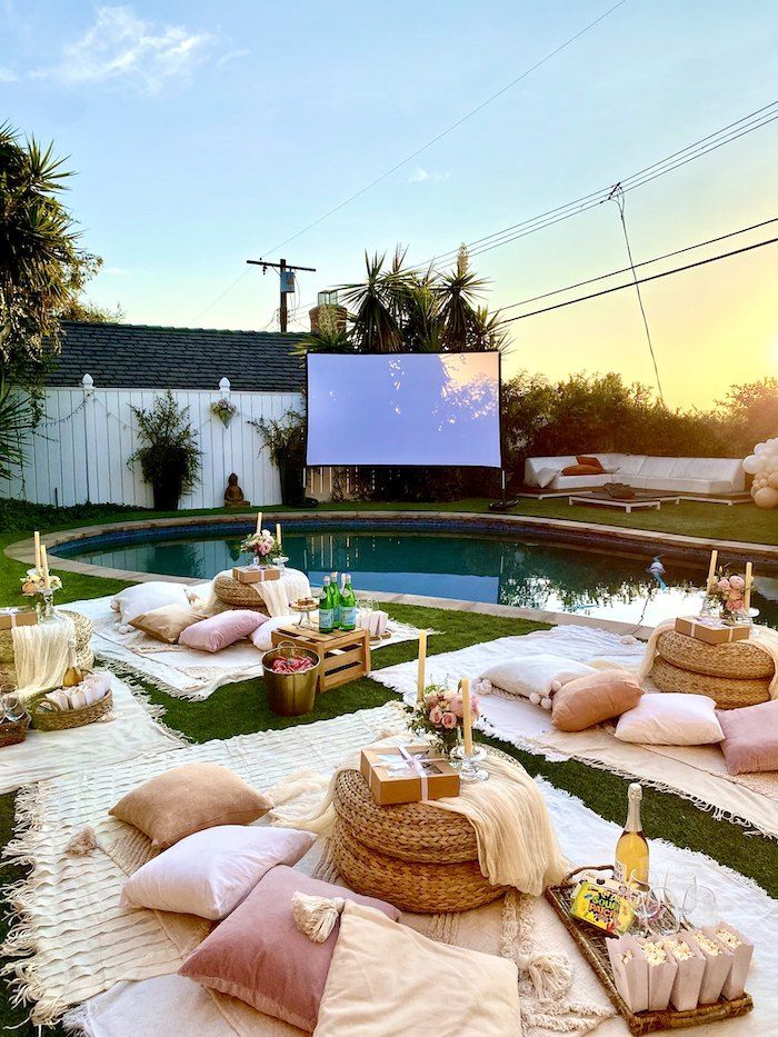 an outdoor movie is set up in the backyard with lots of pillows and blankets on the grass