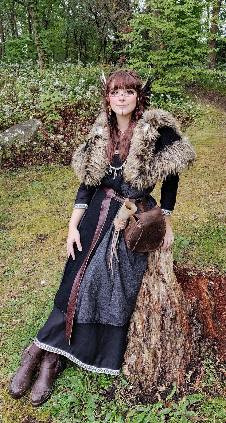 a woman dressed in medieval clothing sitting on top of a tree stump wearing a fur collar