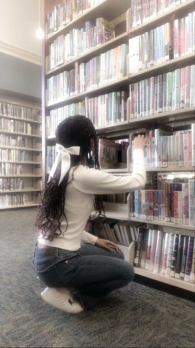 a woman kneeling down in front of a bookshelf filled with lots of books