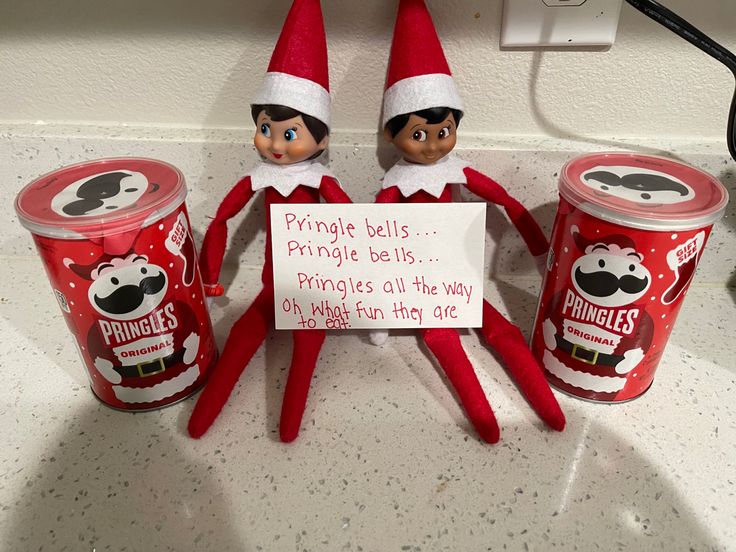 two elfs are sitting on top of three cans of prince bell's pringle bells