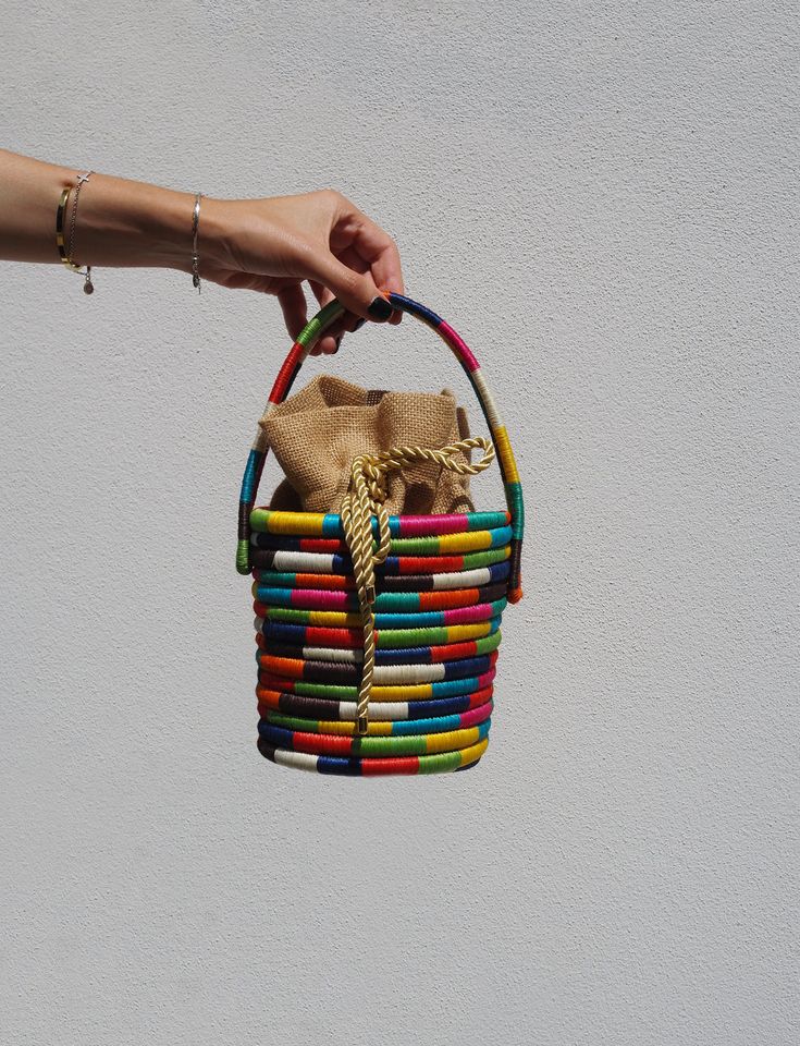 a woman's hand is holding a multicolored basket hanging from the ceiling