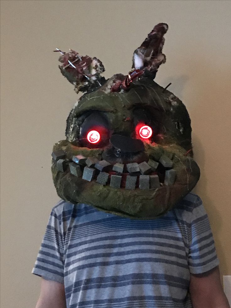 a young boy wearing a creepy mask with red eyes and glowing fangs on his face