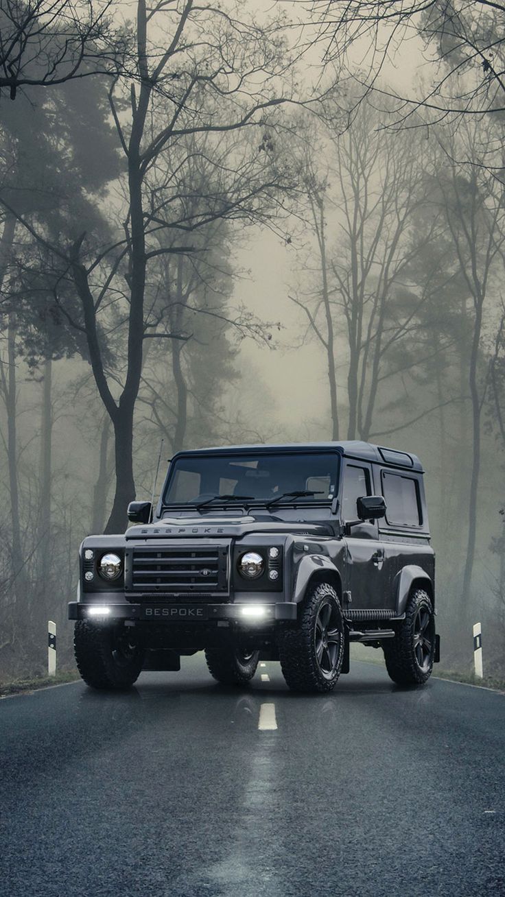 a black land rover is driving down the road in front of some trees and fog