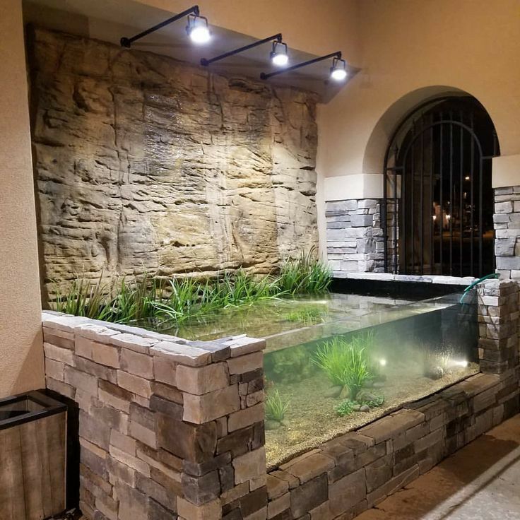 an indoor fish pond in the middle of a room with stone walls and flooring