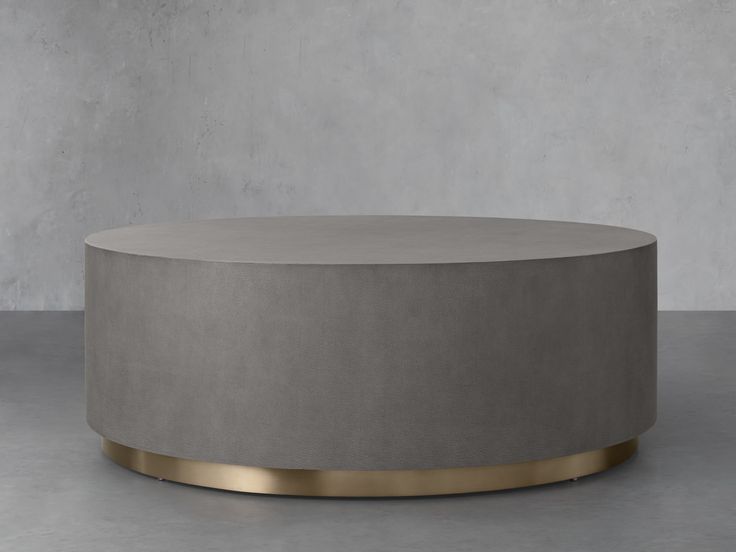 a round concrete coffee table with gold trim around the top and bottom, in front of a gray wall