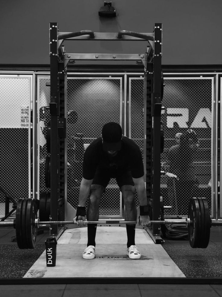 a man squats in front of a barbell with one foot on the ground