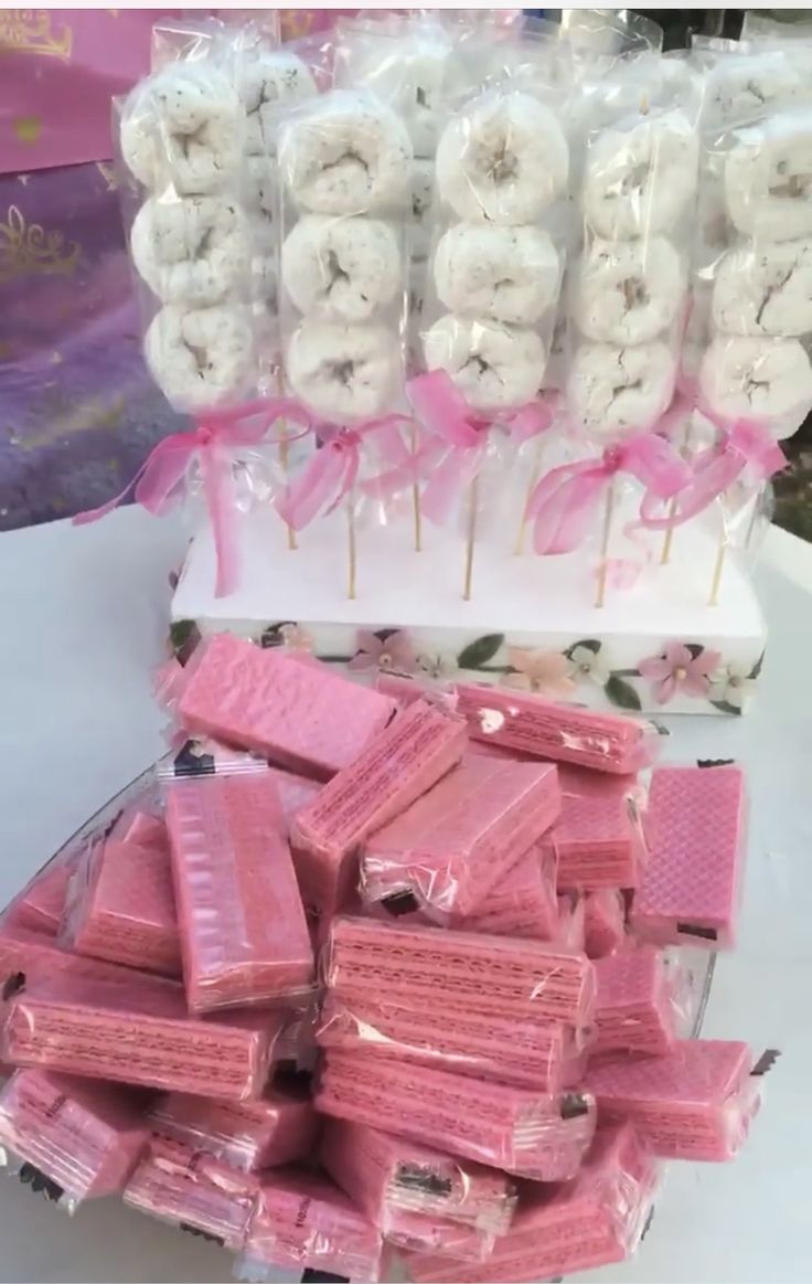 there are many pink and white donuts in the box on the table with ribbons