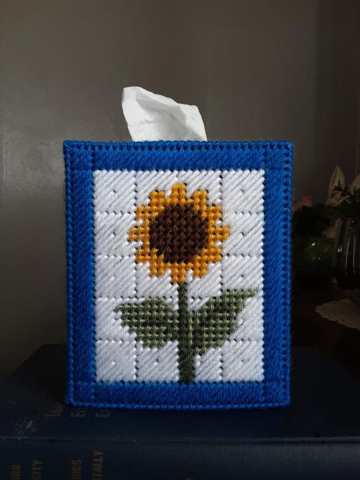 a tissue box with a cross stitch sunflower on it, sitting on top of a blue book