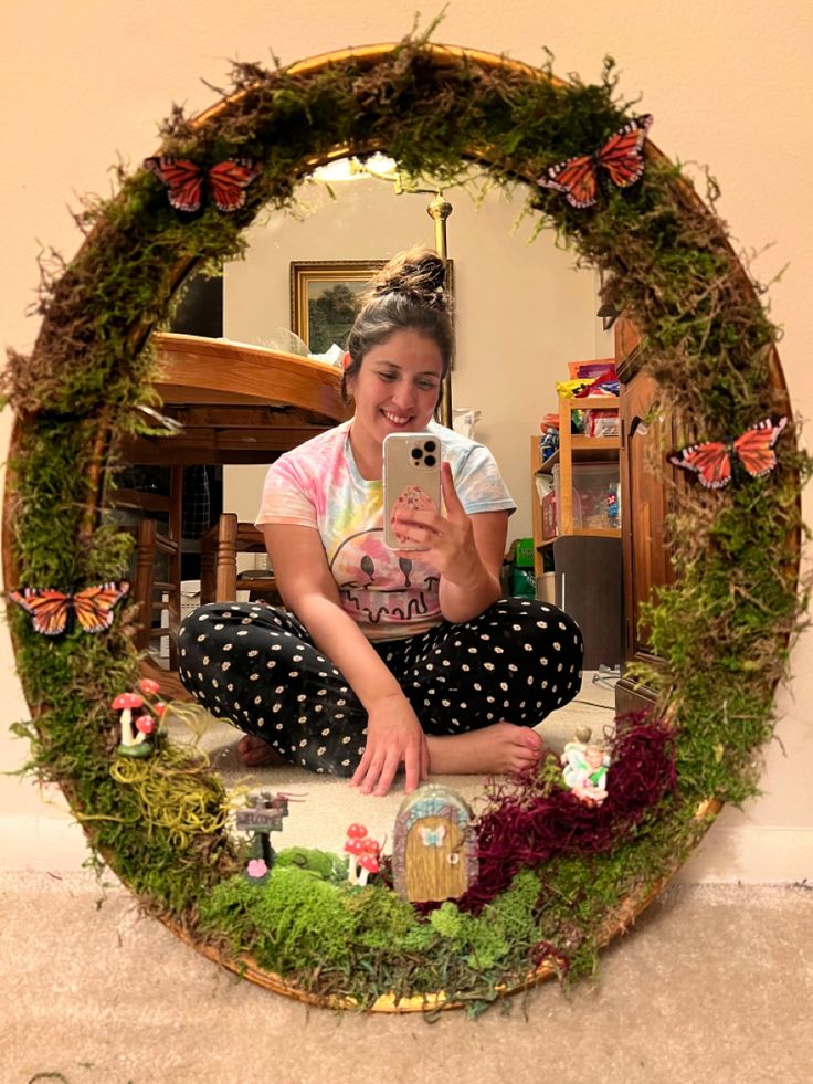 a woman sitting on the floor in front of a mirror with moss growing around it