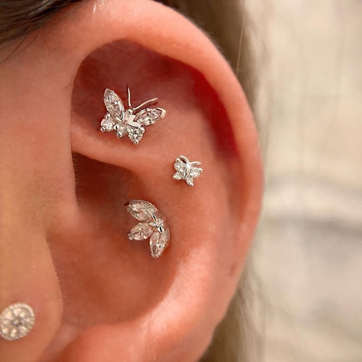 three silver butterfly ear studs on the side of a woman's ear,