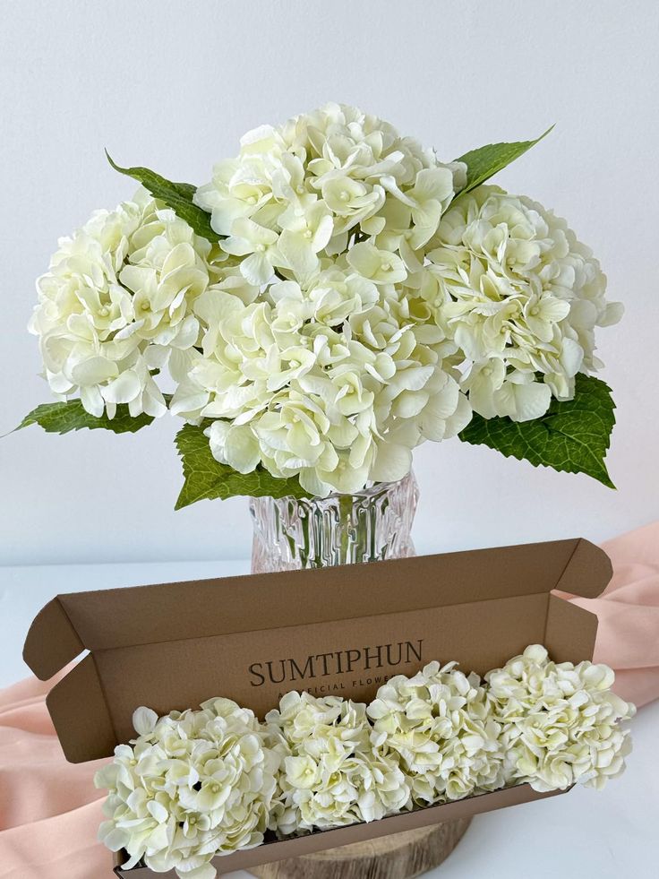 a vase filled with white flowers sitting on top of a table next to a box