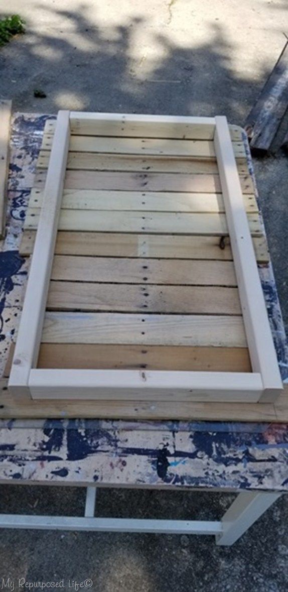 a wooden frame sitting on top of a blue and white paint covered ground next to a tree