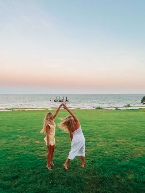 two young women playing with a frisbee on the grass by the ocean at sunset