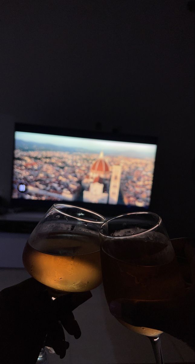 two glasses of wine sitting next to each other in front of a television set with a city scene on the screen