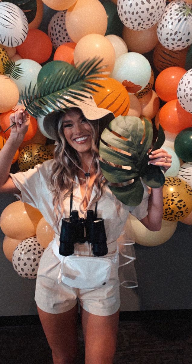 a woman standing in front of a wall with balloons and hats on it's head