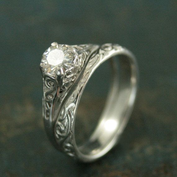 a white gold ring with an intricate design and a single diamond in the center, on a green surface