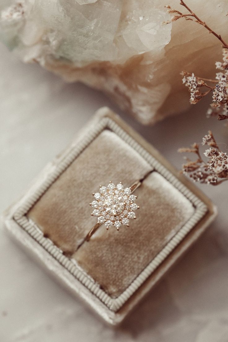 an engagement ring sitting on top of a box next to some rocks and flowers in the background