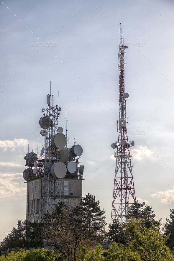 two cell towers with antennas and trees in the foreground