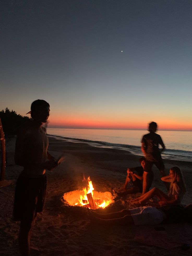 people sitting around a campfire on the beach