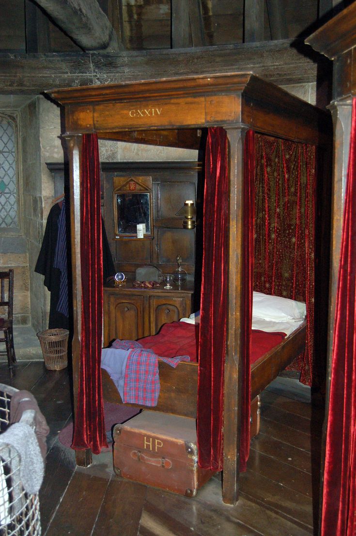 an old fashioned bedroom with red drapes on the canopy bed and wooden flooring