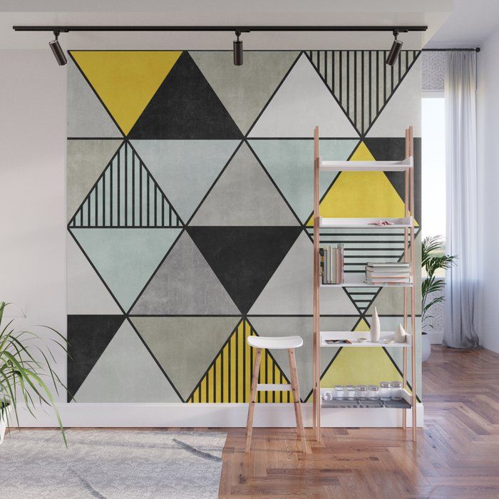 an abstract geometric wall mural with yellow, grey and black triangles on the side in a living room