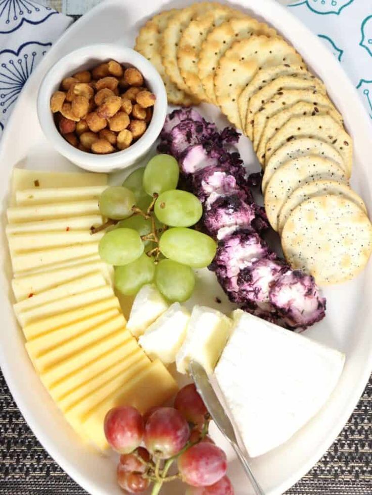 a white plate topped with cheese, crackers and grapes