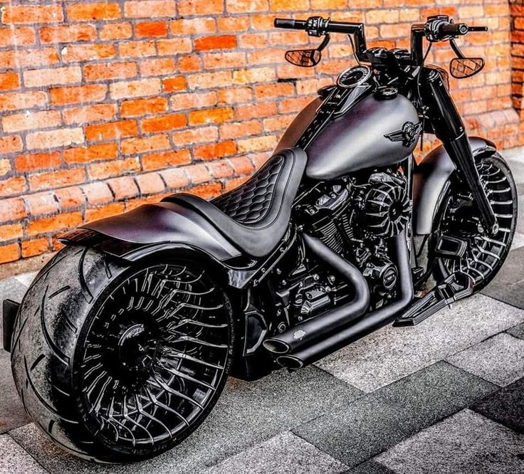 a black motorcycle parked in front of a brick wall on the street with its wheels down