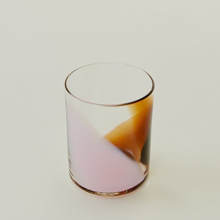 a glass with some liquid in it sitting on a table next to a white wall