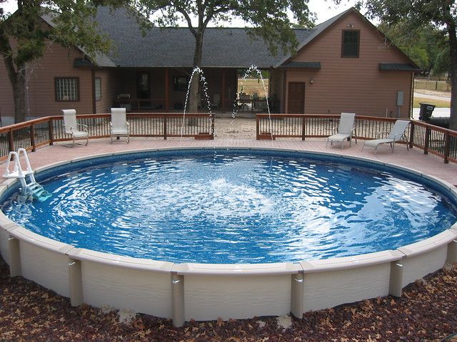 an above ground swimming pool surrounded by trees and gravel with chairs on the decking area