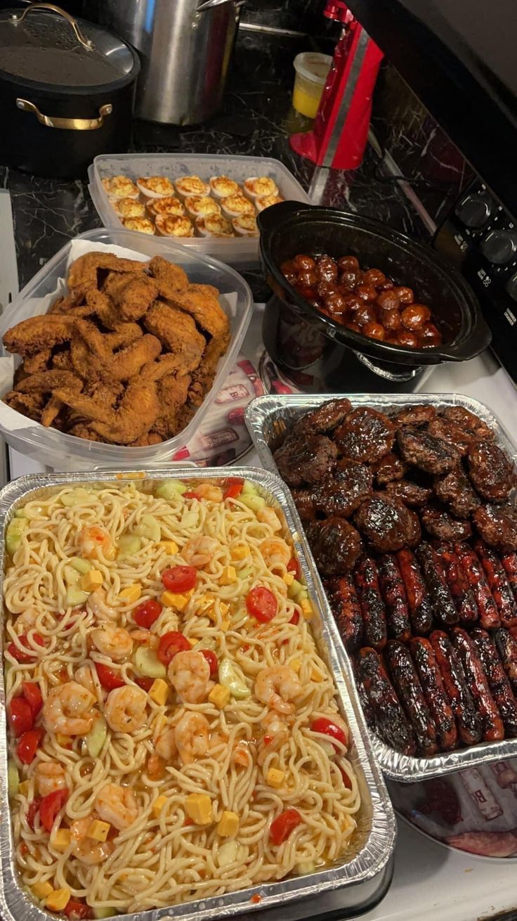 several trays of food on a counter top with utensils and other foods