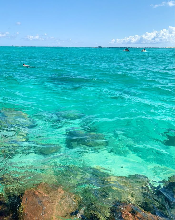 the water is crystal blue and clear with people in boats on the ocean behind them