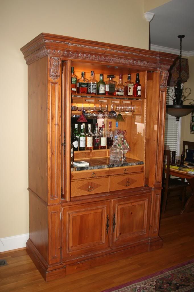 an old fashioned bar with liquor bottles on the top and bottom shelves, in a living room