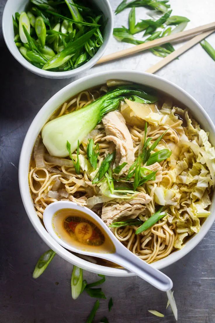 a bowl filled with noodles, meat and veggies next to a small spoon