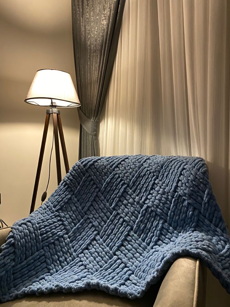 a bed with a blue blanket on top of it next to a lamp and curtains