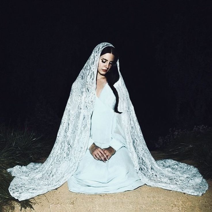 a woman sitting on the ground wearing a blue dress and veil with her hands in her pockets