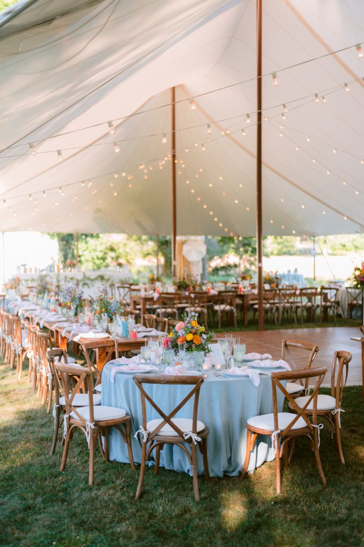 an outdoor tent with tables and chairs set up for a formal dinner or party in the grass