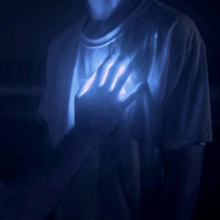 a man in the dark holding his hand up to light it up with blue lights