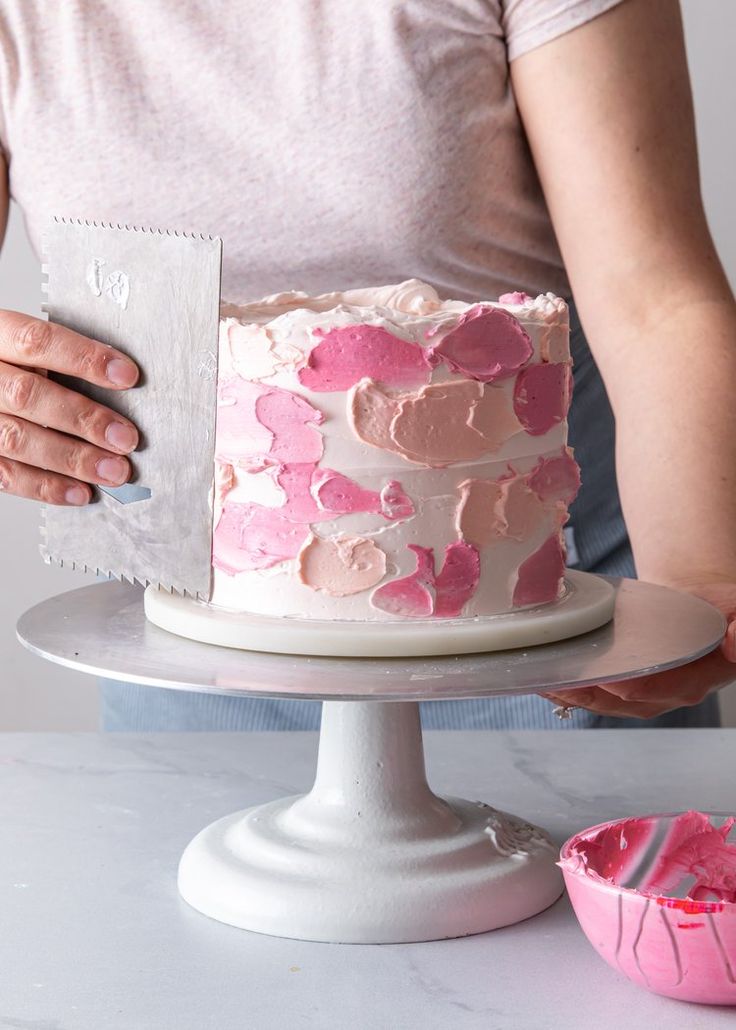 a woman is decorating a cake with pink icing and heart shapes on it