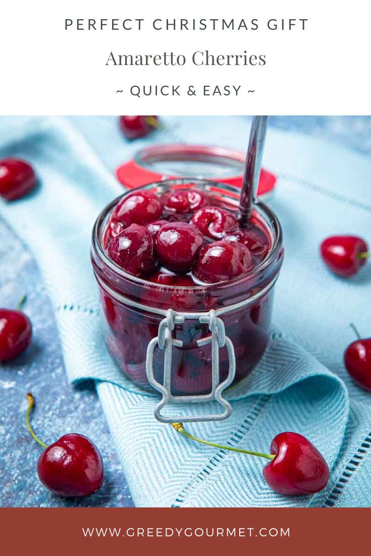 a glass jar filled with cherries sitting on top of a blue cloth next to a spoon